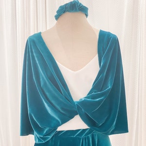 May include: A teal velvet shrug featuring a twisted front design, worn over a white sleeveless top, paired with a matching teal velvet skirt and a coordinating teal velvet knotted headband. The fabric has a soft, reflective sheen throughout.