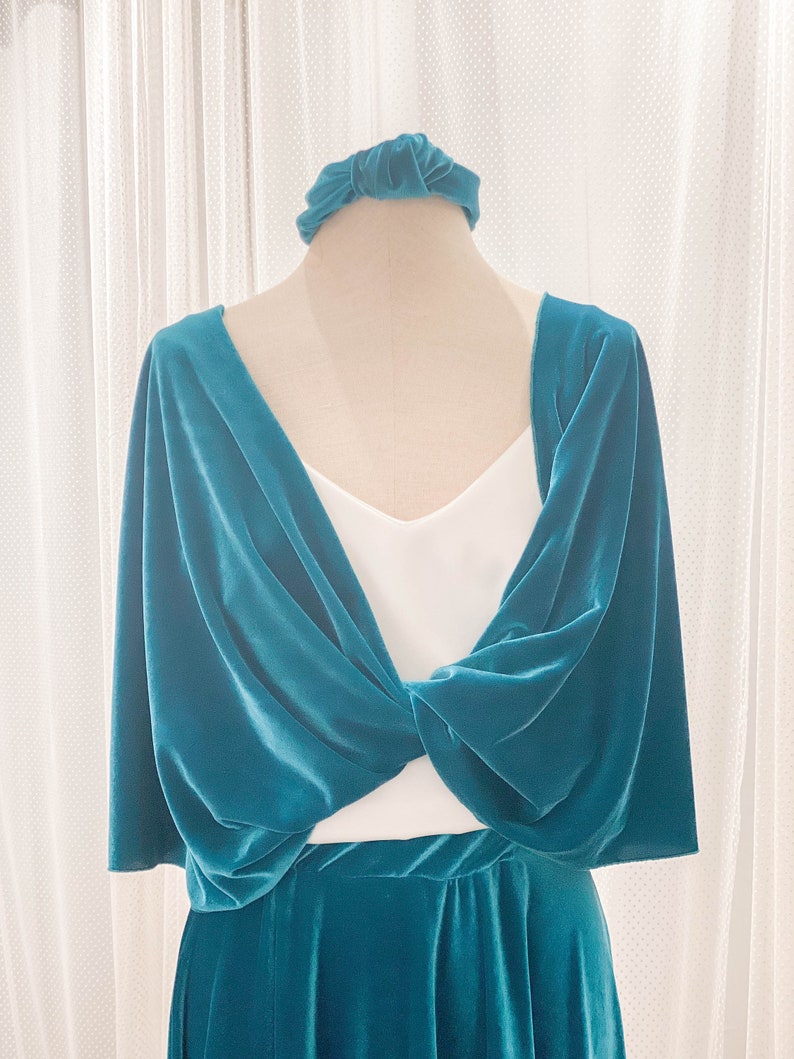 May include: A teal velvet shrug featuring a twisted front design, worn over a white sleeveless top, paired with a matching teal velvet skirt and a coordinating teal velvet knotted headband. The fabric has a soft, reflective sheen throughout.