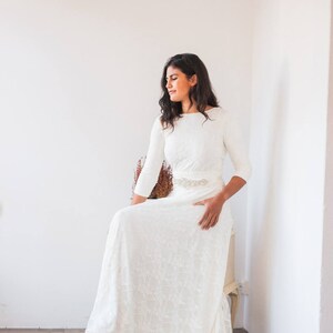 A model dressed like a bride is sitting in a drawer. The gown has a boat neckline, which makes it perfect for a winter wedding because it's warmer than usual. She is wearing also a vintage belt that it's a perfect match