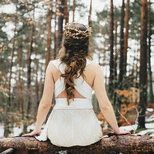 Boho bride sitting in a fallen tree. She is a snowy landscape that looks incredibly calm. She wears a braid over her winter wedding dress, that is crossed in her back