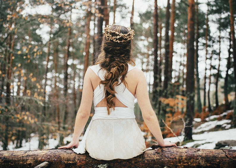 Boho bride sitting in a fallen tree. She is a snowy landscape that looks incredibly calm. She wears a braid over her winter wedding dress, that is crossed in her back