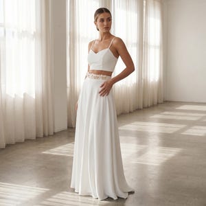 Peut inclure: Un ensemble deux pièces blanc composé d'un haut court sans manches à encolure en cœur et d'une jupe longue trapèze. La jupe présente une ceinture décorative ornée de petites décorations florales de couleur claire.
