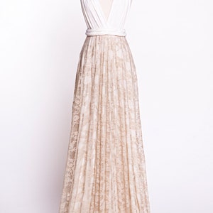 May include: A floor-length gown featuring a solid white sleeveless bodice with a deep V-neckline and thick straps. The waist is cinched with a white band, transitioning into a long, flowing skirt covered in a beige floral lace overlay.