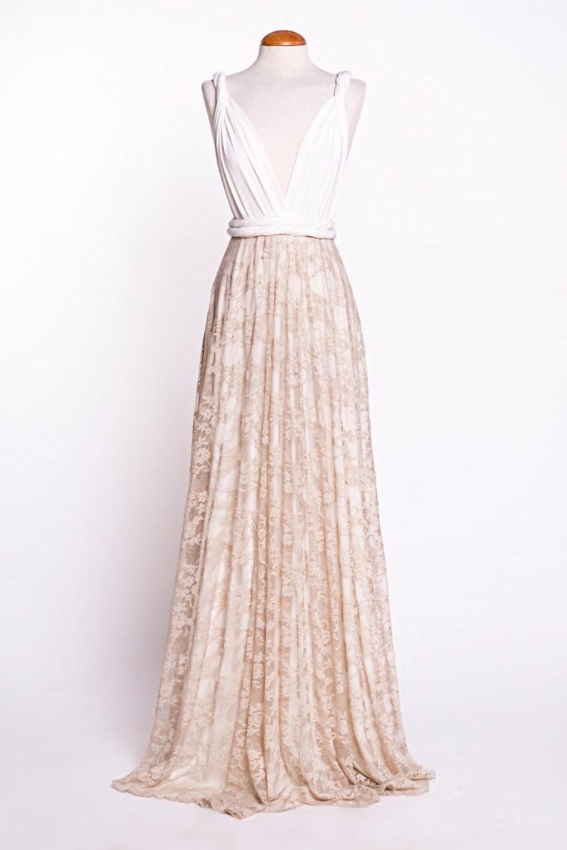 May include: A floor-length gown featuring a solid white sleeveless bodice with a deep V-neckline and thick straps. The waist is cinched with a white band, transitioning into a long, flowing skirt covered in a beige floral lace overlay.