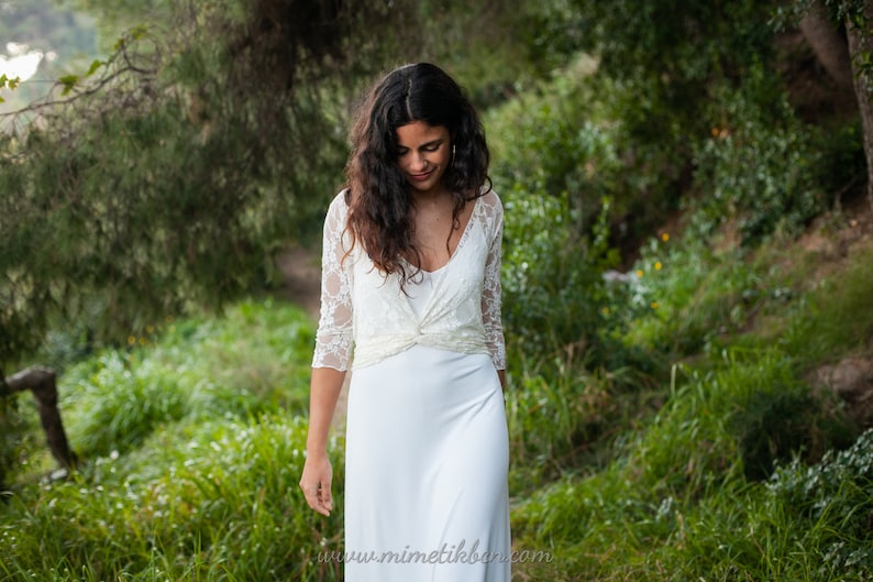 The model is wearing the same simple wedding dress with an elegant ivory lace bolero. The bolero is convertible, so it can be worn in different ways. She has wrapped it with deep v-neck.