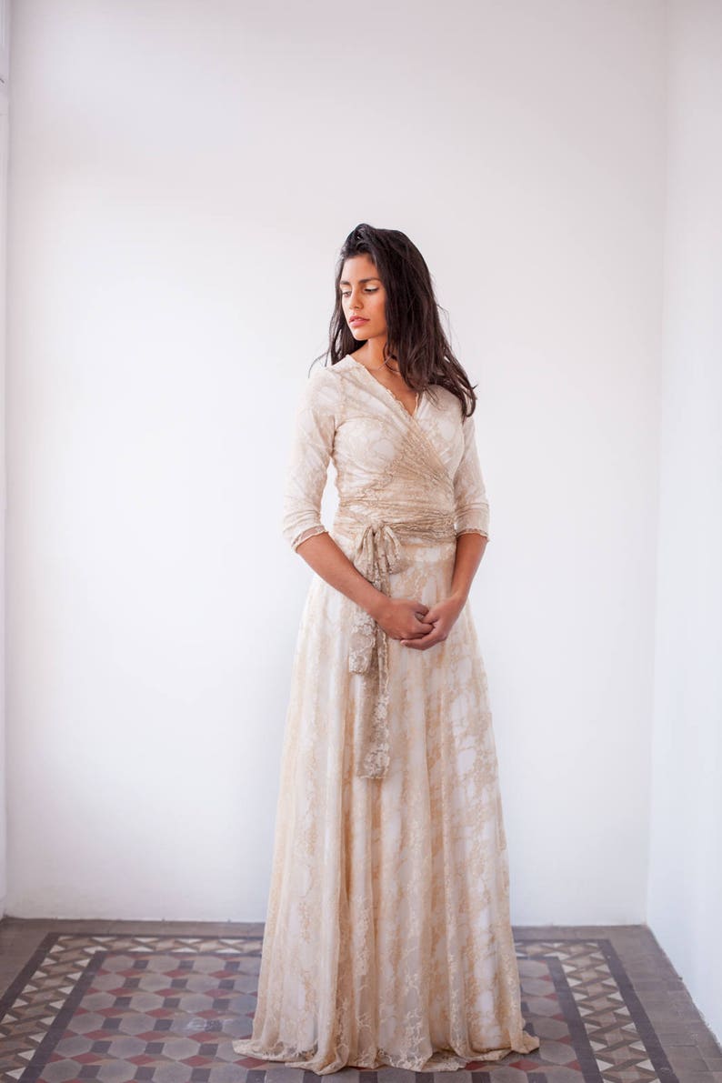 Lovely woman staring in a room wearing a bridal gown in golden lace with 3/4 sleeves