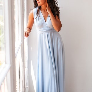 Curly woman with a long dress in a soft serenity blue looking through the window.