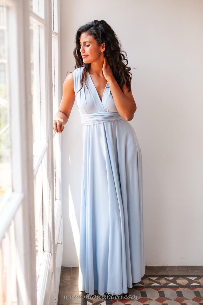 Curly woman with a long dress in a soft serenity blue looking through the window.