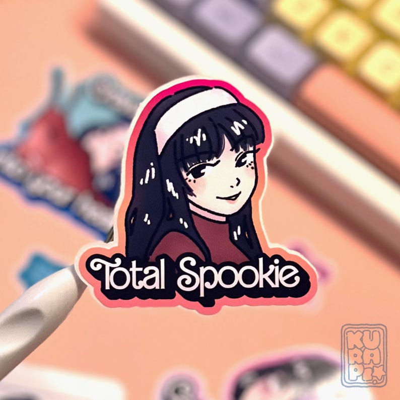 a gradient orange + pink background sticker depicting Tomie from the manga by Junji Ito, smiling,  with the "total spookie" writing below.