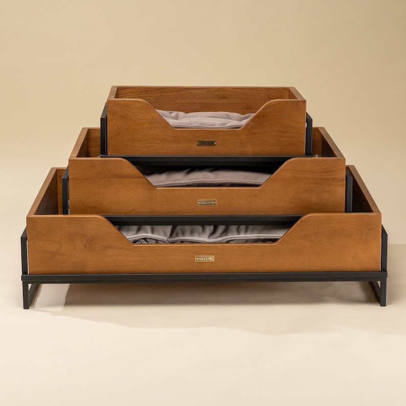 May include: A wooden dog bed with a black metal frame. The bed is made up of three tiers, each with a gray cushion.