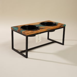 May include: Double dog bowl stand made of wood with a teal epoxy resin inlay. The stand has a black metal frame.