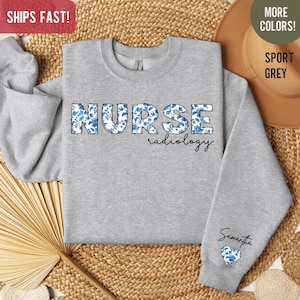 May include: A gray sweatshirt with the words "NURSE radiology" printed on the front. The letters are decorated with a blue and white floral pattern. The sweatshirt has a small heart with the same floral pattern on the sleeve and the name "Samantha" written above it.