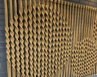 May include: A wall hanging made of woven macrame cord in a natural beige color. The cord is knotted in a repeating pattern to create a geometric design.