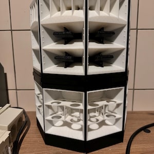 Puede incluir: Un altavoz hexagonal blanco y negro con múltiples puertos de sonido. El altavoz está hecho de plástico y tiene un diseño moderno.