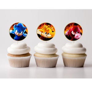 May include: Three cupcakes with edible images of Sonic the Hedgehog characters. The cupcakes are white with yellow frosting. The images are of Sonic, Tails, and Knuckles. The images are in a circle with a gold border.
