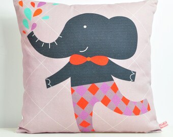 Peut inclure: Un coussin rose avec une illustration noire et blanche d'un éléphant portant un nœud papillon rouge et un pantalon à carreaux. L'éléphant arrose de l'eau avec sa trompe.