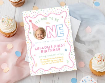 May include: A birthday invitation with the text "It's Fun to be One" and a photo of a child wearing a party hat. The invitation is decorated with pastel colors and confetti, with cupcakes in the background.