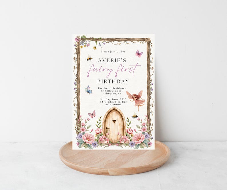 Puede incluir: Una invitaci&oacute;n de cumplea&ntilde;os con tem&aacute;tica de hadas. La invitaci&oacute;n presenta una puerta de madera con un coraz&oacute;n, rodeada de flores, mariposas y abejas. El texto dice "Averie's fairy first birthday". La invitaci&oacute;n est&aacute; sobre una bandeja de madera.