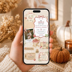 May include: A smartphone screen displaying a digital baby shower invitation with a beige gingham background. The design features red apple illustrations, a photo frame, and text including "the APPLE of our eye" and "OLIVIA SMITH" with event details.