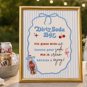 May include: A gold-framed sign with a light blue striped background featuring the text Dirty Soda Bar. The sign includes instructions to fill glass with ice, choose your soda, mix in cream, and garnish and enjoy, with illustrations of a cola bottle, cherries, and a candy cane.