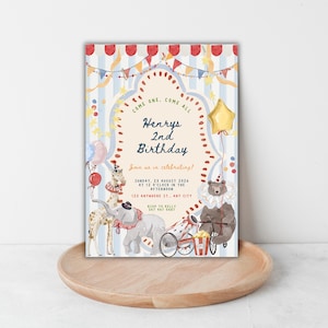 May include: A rectangular birthday invitation card featuring a circus theme with light blue stripes, red and white scalloped trim, and colorful bunting. Illustrations include a giraffe, elephant, and bear in clown collars, a cannon, and a star balloon.