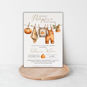 May include: Baby shower invitation with a watercolor design. The invitation features a pumpkin, baby clothes, and the text "A Little Pumpkin is on the Way." The invitation is for Olivia Wilson's baby shower on October 15th.