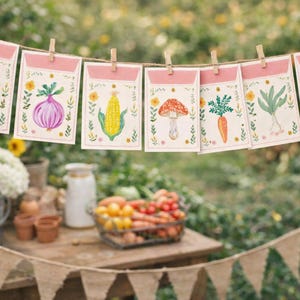 Puede incluir: Una guirnalda de tarjetas decorativas de sobres de semillas, cada una con una ilustración de un vegetal diferente. Las tarjetas están sujetas con pinzas de madera en una cuerda. Los vegetales incluyen una cebolla roja, maíz y un hongo.