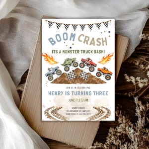 Puede incluir: Una tarjeta de invitación de cumpleaños rectangular con temática de camiones monstruo, cuatro camiones coloridos, banderas a cuadros, llamas y huellas de neumáticos. El texto dice BOOM CRASH ITS A MONSTER TRUCK BASH HENRY IS TURNING THREE JUNE 13 2 PM HENRY'S HOUSE 123 ANYWHERE ST ANY CITY RSVP TO KELLY 404-585-4572.