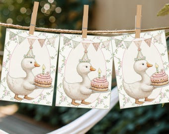 May include: Three printable cards featuring a white duck wearing a party hat and holding a pink and white frosted cupcake with a lit candle. The cards have a green and white floral border with pink and white bunting.