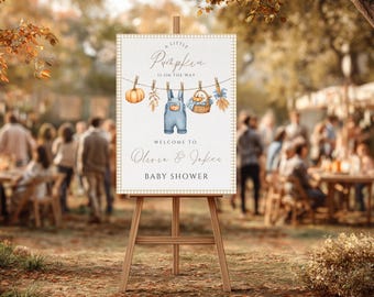 May include: A baby shower sign on a wooden easel. The sign features a pumpkin, overalls, and a basket illustration. Text reads "A Little Pumpkin Is On The Way" and "Welcome to Olivia & Jake's Baby Shower."