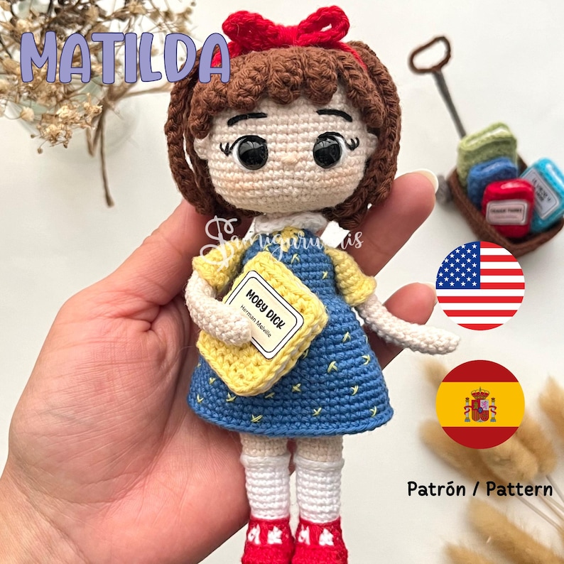 May include: A handmade crochet doll of a girl in a blue dress, holding a yellow book labeled "Moby Dick." The doll has brown hair, a red bow, and red shoes. The word "MATILDA" is above the doll in the image.