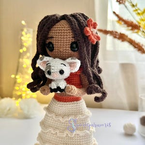 May include: Crocheted doll with brown hair and a red flower in her hair. She is holding a white crocheted pig in her arms. The doll is wearing a white crocheted skirt with a red crocheted belt.