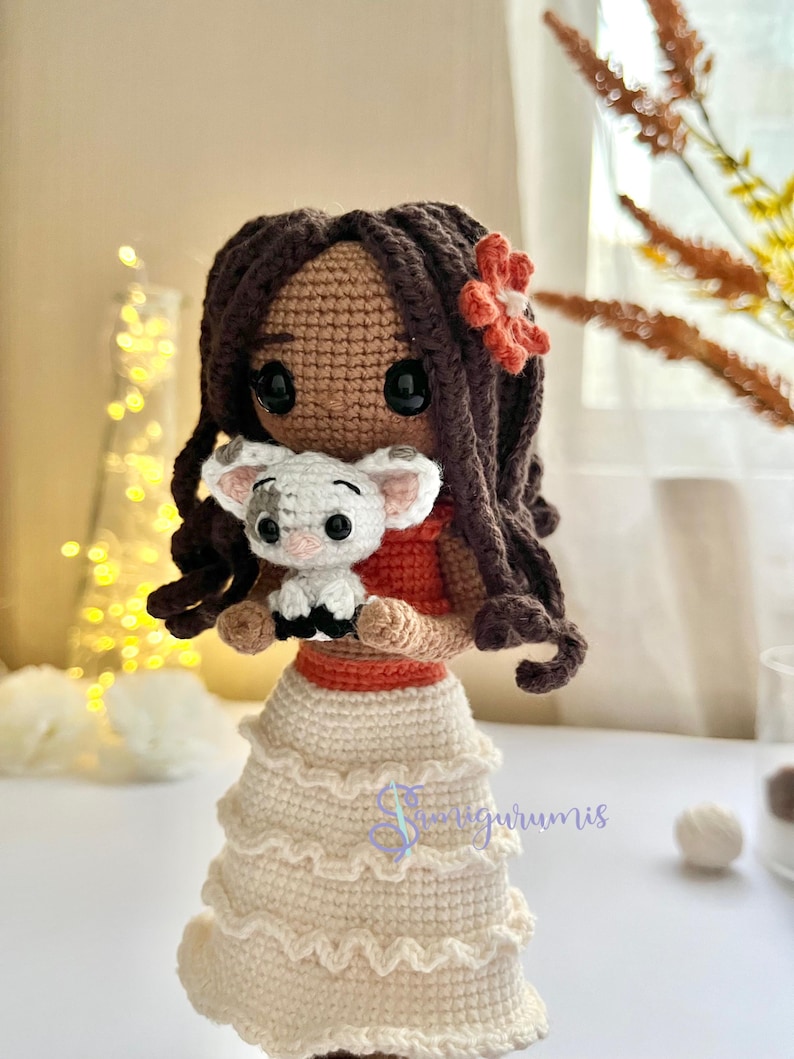 May include: Crocheted doll with brown hair and a red flower in her hair. She is holding a white crocheted pig in her arms. The doll is wearing a white crocheted skirt with a red crocheted belt.