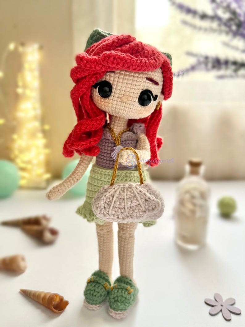 May include: A handmade crochet doll with red hair, green accents, and a light green dress. The doll has a small purse and green sandals. The doll is a whimsical, handcrafted item.
