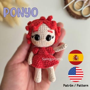 Puede incluir: Una muñeca amigurumi de crochet de Ponyo de la película Ponyo. La muñeca lleva un vestido rojo y tiene el pelo rojo. La muñeca está levantando un brazo. La imagen también incluye el texto "Patrón / Pattern" y banderas de España y Estados Unidos.