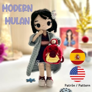 Puede incluir: Muñeca de crochet con cabello negro, vistiendo un vestido azul y rosa y una chaqueta gris. La muñeca lleva una mochila de crochet roja y amarilla con un diseño de dragón. La imagen también incluye el texto "Patrón / Pattern" y banderas de España y Estados Unidos.