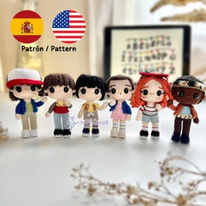 Puede incluir: Seis muñecos de ganchillo, cada uno representando un personaje con peinados y ropa distintos. Los muñecos están colocados en fila. La imagen incluye el texto "Patrón / Pattern" y las banderas de España y Estados Unidos. Los muñecos tienen diferentes tonos de piel.