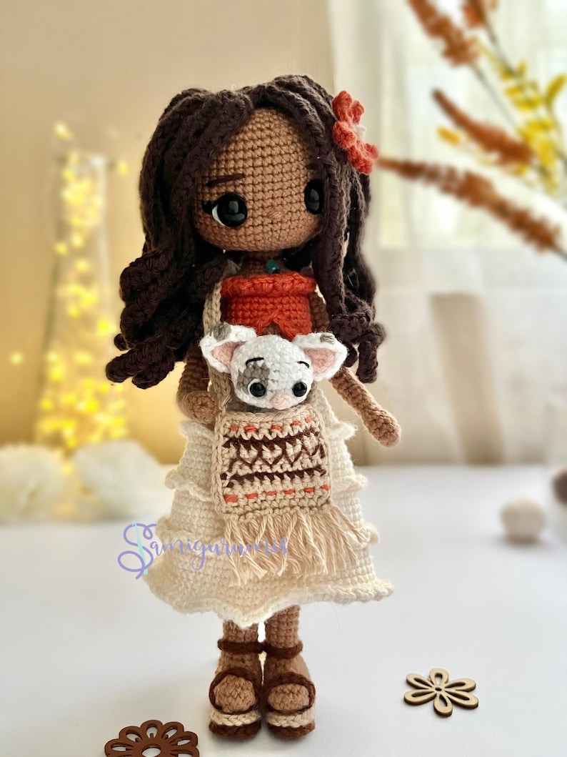 May include: Crocheted doll with brown hair, wearing a white dress with a brown and orange patterned vest, holding a small white crocheted animal.