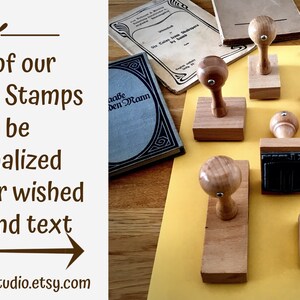 Puede incluir: Una colecci&oacute;n de ocho sellos de madera con mangos redondos. Los sellos est&aacute;n dispuestos sobre una superficie amarilla. Los sellos son para personalizar ex libris con un nombre y un texto.