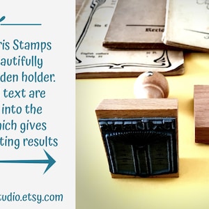 Puede incluir: Dos bloques de sellos de madera con un mango de madera tallado. Los bloques de sellos est&aacute;n sobre una superficie amarilla. Los bloques de sellos tienen un sello de goma negro con un dise&ntilde;o de un libro con un borde decorativo. El texto en el sello dice "Ex Libris".