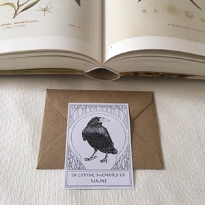 Pu&ograve; includere: Un biglietto bianco con un'illustrazione in bianco e nero di un corvo in una cornice decorativa. Il biglietto dice "In memoria affettuosa di NAME".