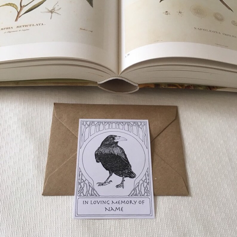 Pu&ograve; includere: Un biglietto bianco con un'illustrazione in bianco e nero di un corvo in una cornice decorativa. Il biglietto dice "In memoria affettuosa di NAME".