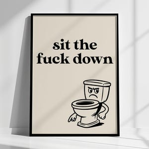 Könnte beinhalten: Schwarz gerahmter Kunstdruck mit dem Text "sit the fuck down" über einer Cartoon-Toilette mit wütendem Gesicht. Das Kunstwerk befindet sich auf beigem Hintergrund.