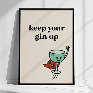 May include: A framed print with the words "keep your gin up" in black text. A cartoon gin glass with a red cape and raised fist is flying upwards. The background is a light beige color.