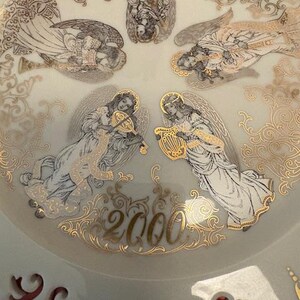 Op de afbeelding: Een decoratieve plaat met een lichtgroene achtergrond, met gouden en witte engelillustraties. De engelen bespelen muziekinstrumenten en zijn omgeven door gouden filigraan. Het jaar "2000" is in goud geschreven.