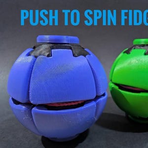May include: Two spherical fidget toys, one blue and one green, featuring segmented outer shells and black top caps. The text PUSH TO SPIN FIDGETS is displayed in blue above the objects. The toys have a visible internal pink core.