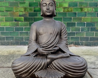 May include: A dark gray stone Buddha statue sitting in a meditative pose with hands in lap. The statue has a gold dot on the forehead.