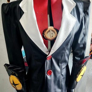 Op de afbeelding: Een zwart leren jack met een witte kraag en rode knopen. Het jack heeft een stervormig ontwerp op de mouwen.