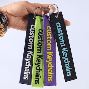 May include: A collection of custom keychains in navy, green, purple, and black. Each keychain features the text "custom Keychains" in a contrasting color. The keychains are attached to silver key rings.