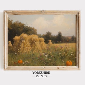 May include: A framed painting of a rural landscape with hay bales in a field of wildflowers. The sky is a soft blue with white clouds. There are two pumpkins in the foreground.
